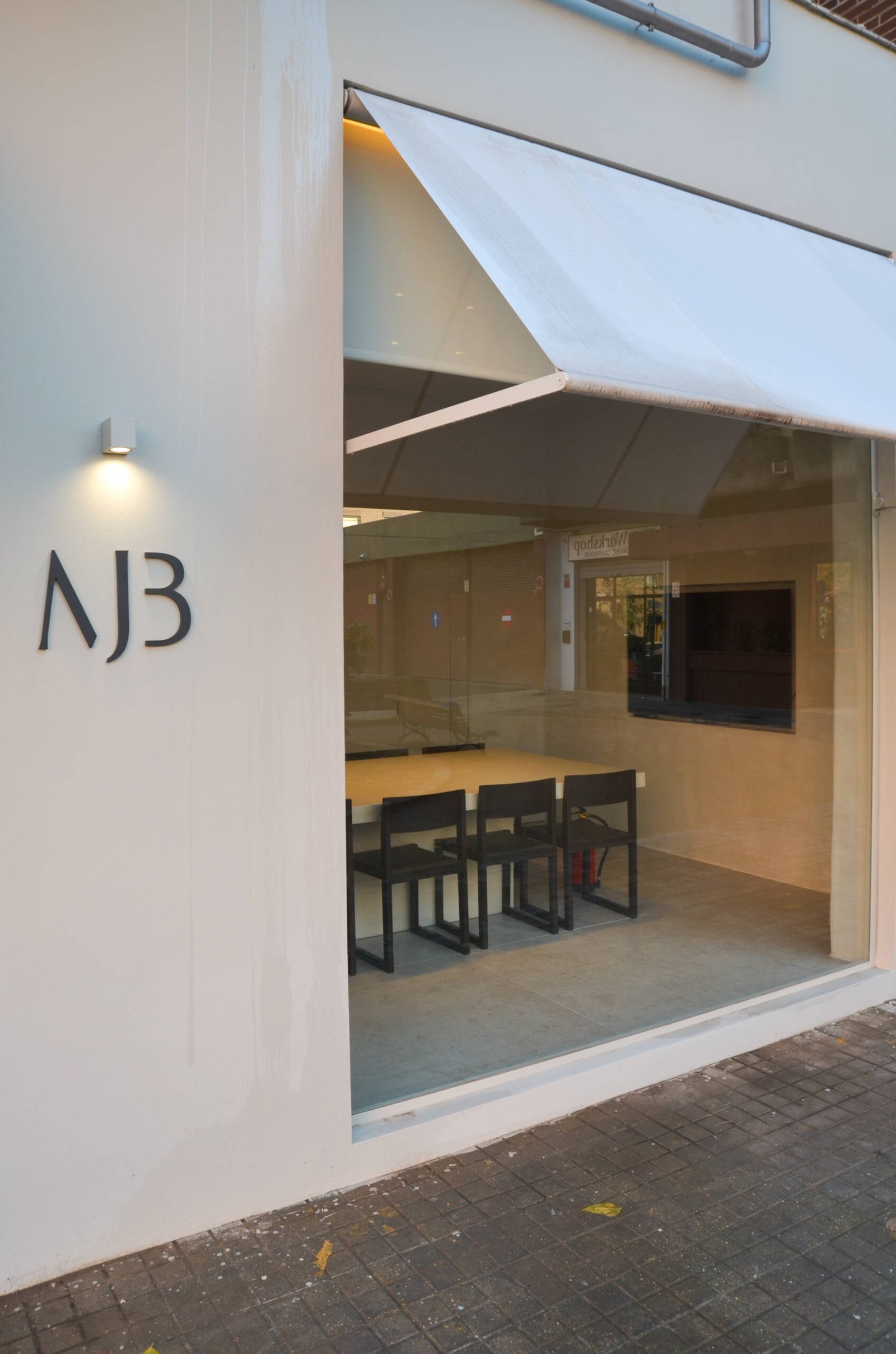 Fachada exterior de la clínica dental de la Dra. María Jesús Bello de noche, mostrando un gran ventanal y su logo elegantemente iluminado por un foco superior, especializada en estética dental conservadora.